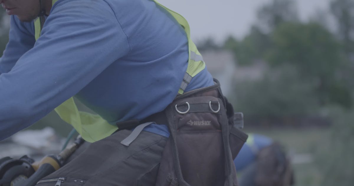 Roofer in a safety vest and tool belt at work