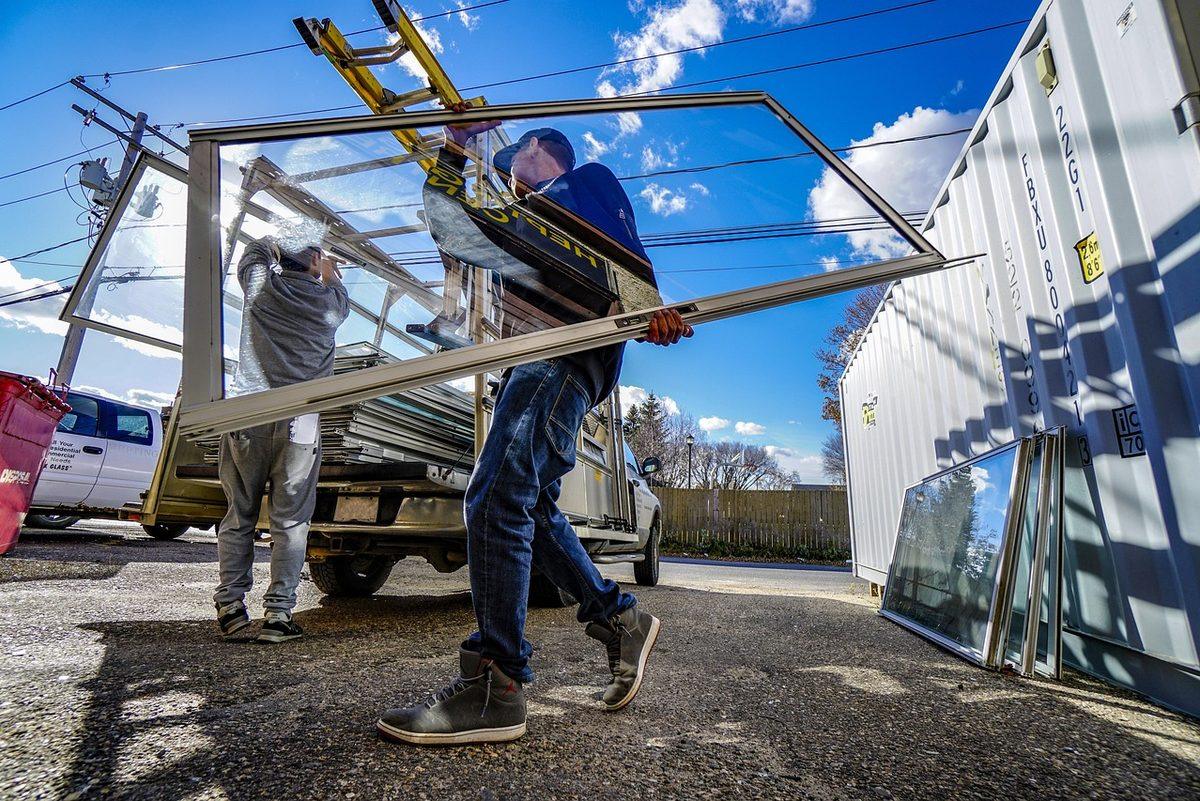 Two workers carrying a large window frame from a truck on a job site
